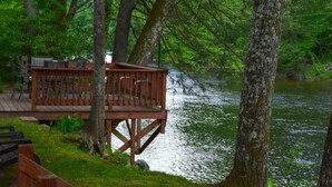 A wooden deck with chairs overlooking a calm river, surrounded by trees. - River’s Edge Cabin- Perfect for Romance/Outdoor Adventures/Relaxation (Elkins)