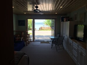A room with a ceiling fan, a television, a dining area with a table and chairs, and a view of the outdoors.