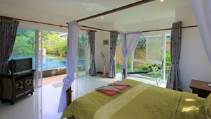 A bedroom with a bed, a TV, and a view of a swimming pool. - Villa Mukdara (Rawai)