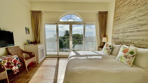 A hotel room with a large bed, a chair, a table, a TV, and a balcony with a view of the sky and greenery. - Spoondrift Hostal (Hengchun)
