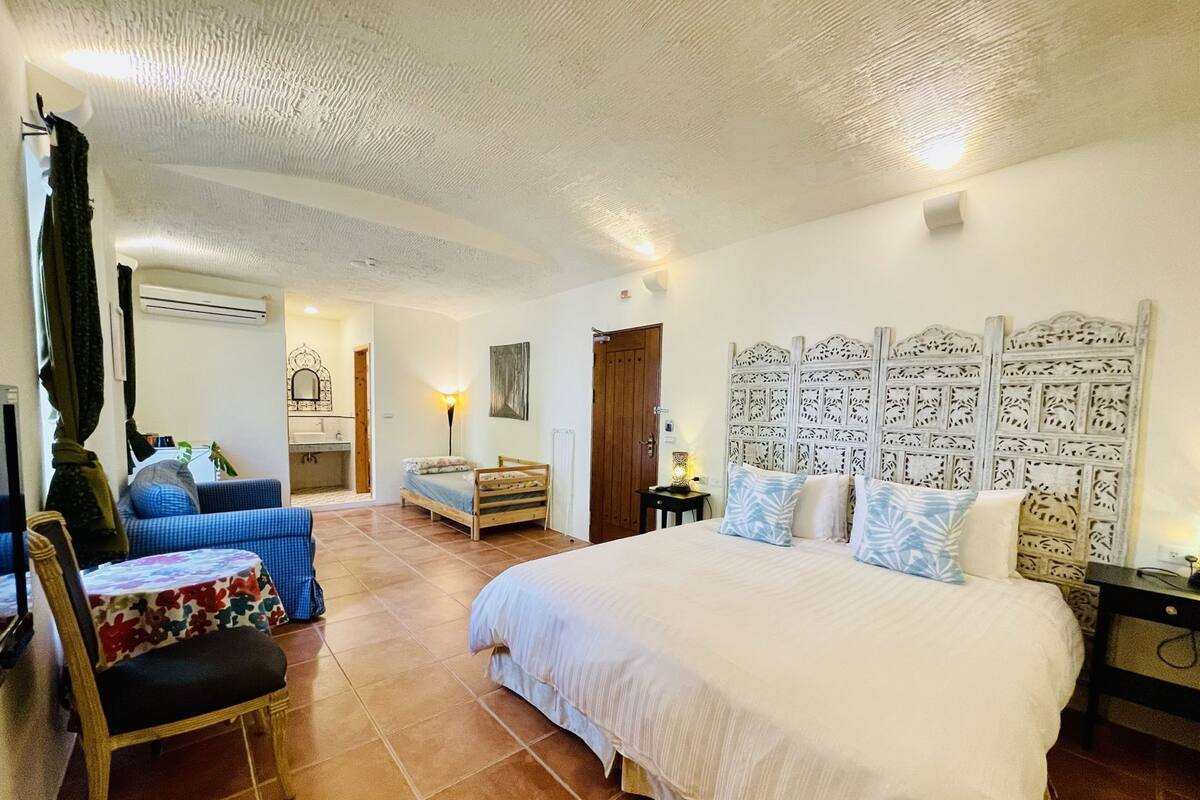 Un dormitorio con una cama grande, una silla, un sofá y un baño visible al fondo.