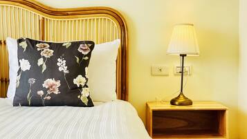 A bed with striped bedding, a floral pillow, a bedside lamp, and a wooden nightstand with a woven basket.