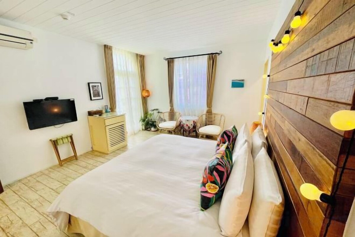 A hotel room with a bed, a television, a desk with a chair, and a wooden headboard with lights.