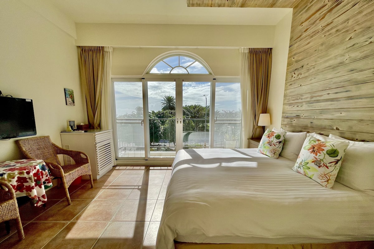 Habitación de hotel con cama, una silla, una mesa, televisor y balcón con vistas.