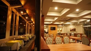 Un restaurant amb diverses taules i cadires, grans finestres i una catifes amb un disseny decoratiu.