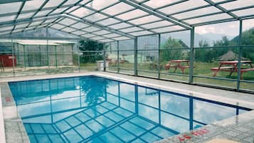 An indoor swimming pool with a glass ceiling, surrounded by a fenced area with picnic tables.