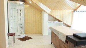 Habitació amb sostre de fusta, una massatge, una zona de dutxa i un petit tamboret.
