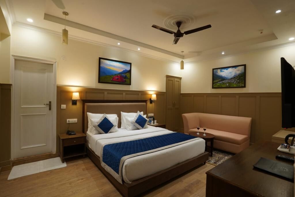 A hotel room with a bed, a sofa, a desk, and two paintings on the wall.