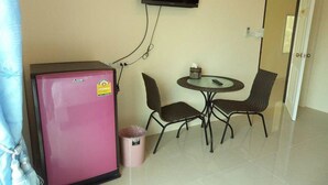 Une petite pièce avec un réfrig érateur rose, un téléviseur fixé au mur, une table ronde avec deux chaises, et une porte au fond.