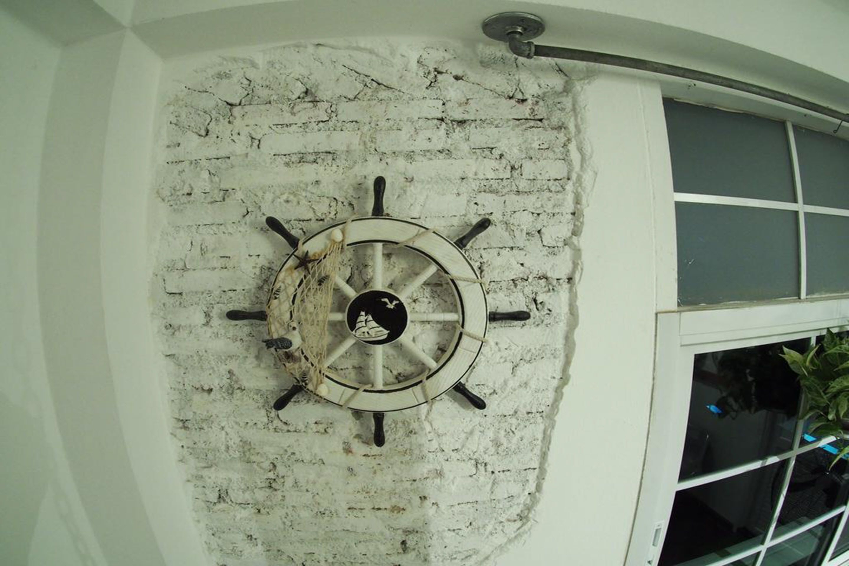 A ship's wheel mounted on a textured wall near a window.