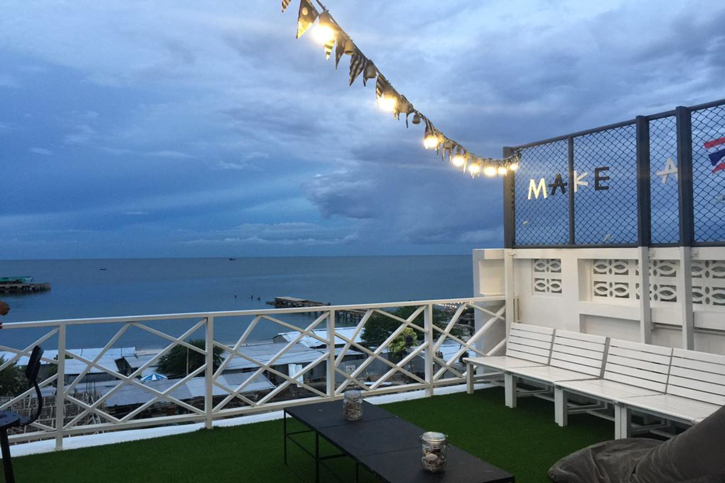 Une terrasse avec vue sur la mer, des sièges blancs et une guirlande lumineuse décorative.