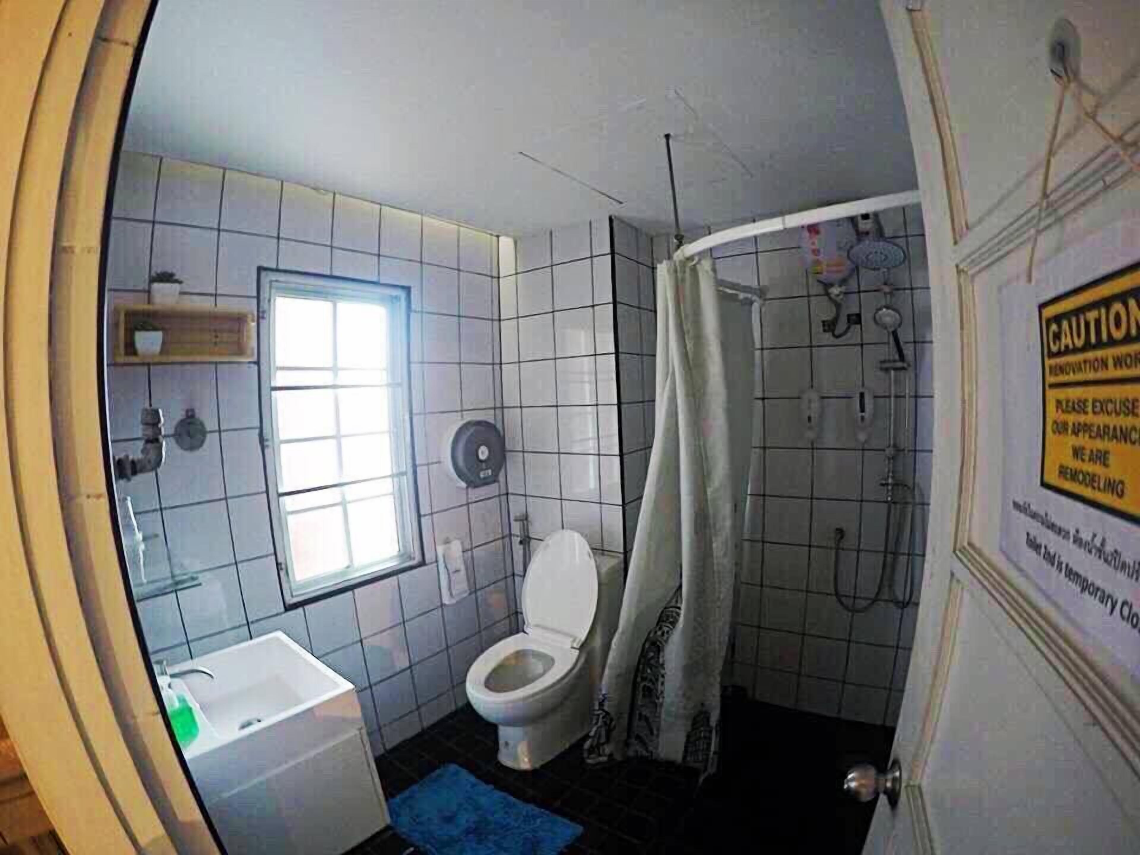 Une salle de bain comprenant des toilettes, un lavabo et un espace douche. Un panneau d’avertissement indique que des travaux de rénovation sont en cours.