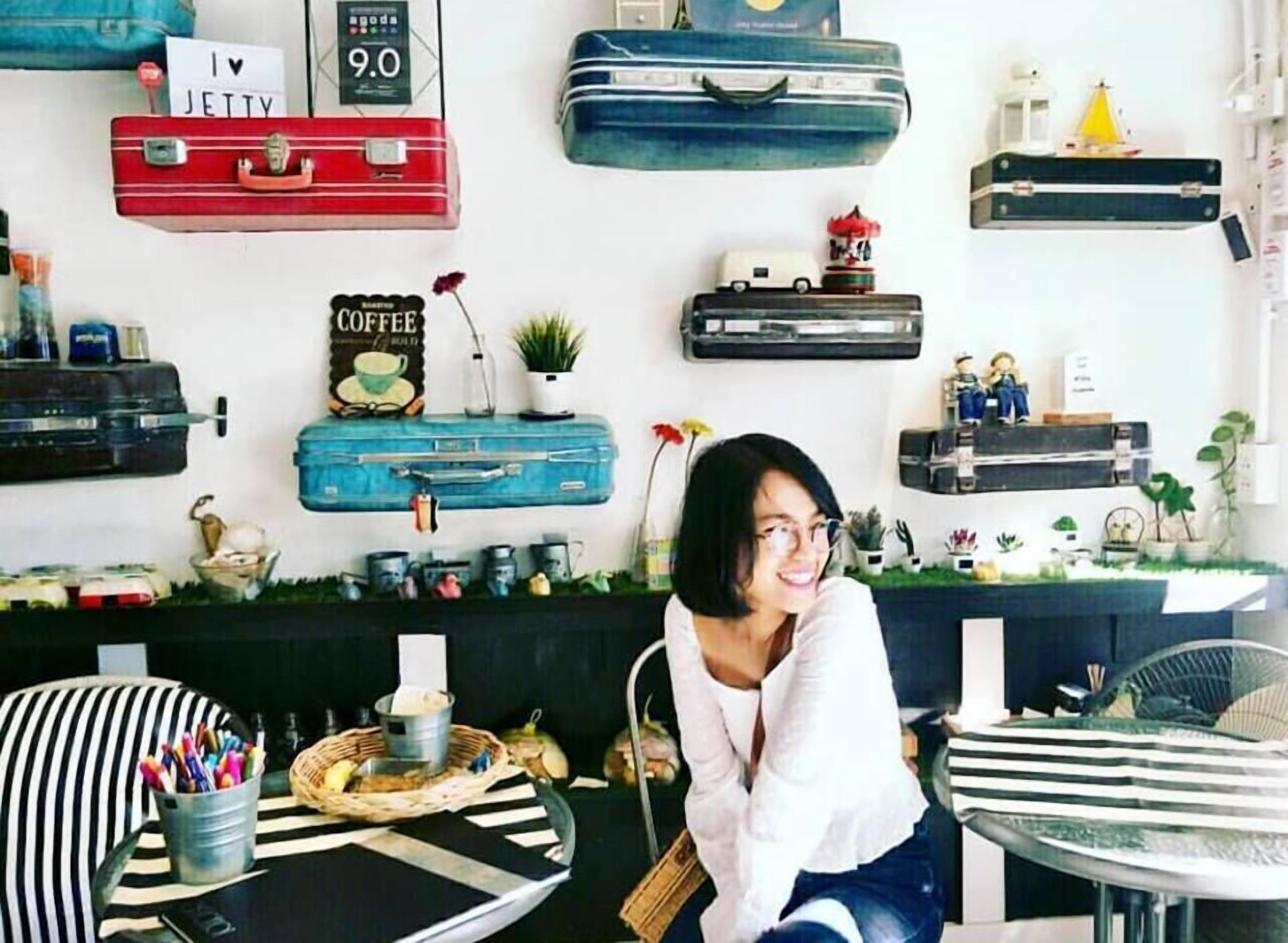Quarto com parede decorada com malas antigas, um letreiro de café e vários objetos decorativos.