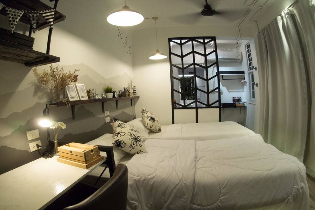 A modern bedroom with a bed, bedside tables, and a desk. There is a decorative wall with a mountain design and a hanging light fixture.