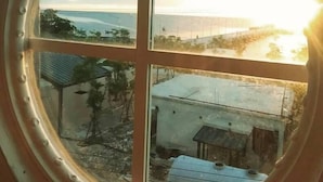 A view through a circular window with a four-pane design, overlooking a coastal area with buildings and vegetation. - Jetty Huahin Hostel (Hua Hin)