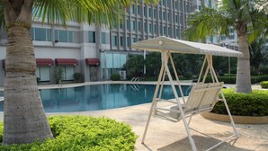 A poolside area with a swing chair, palm trees, and a building in the background. - Bolton Hotel Dongguan (Dongguan)