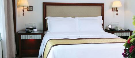 A hotel room with a large bed, two bedside tables, a nightstand, a lamp, and a flower arrangement.