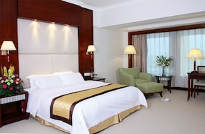 A hotel room with a large bed, two bedside tables, a green armchair, a small table with a vase, and a window with curtains. - Bolton Hotel Dongguan (Dongguan)