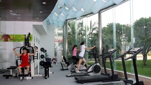 A gym with exercise equipment, large windows, and a view of greenery outside. - Bolton Hotel Dongguan (Dongguan)