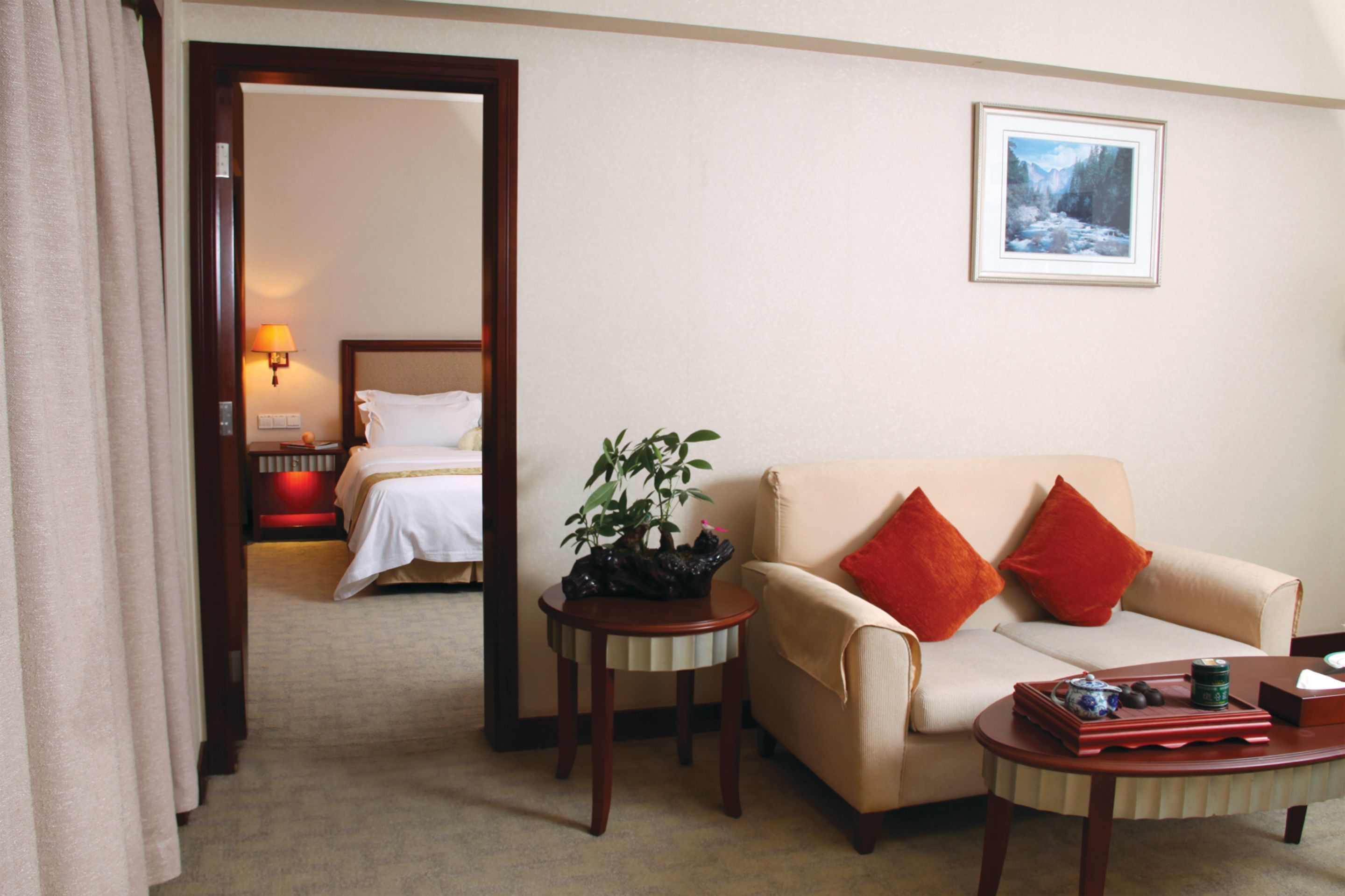 A hotel room with a bed, a sofa, a small table with a plant, and a painting on the wall.