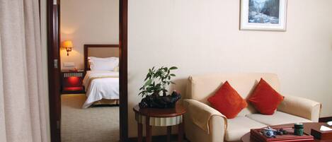 A hotel room with a bed, a sofa, a small table with a plant, and a painting on the wall.