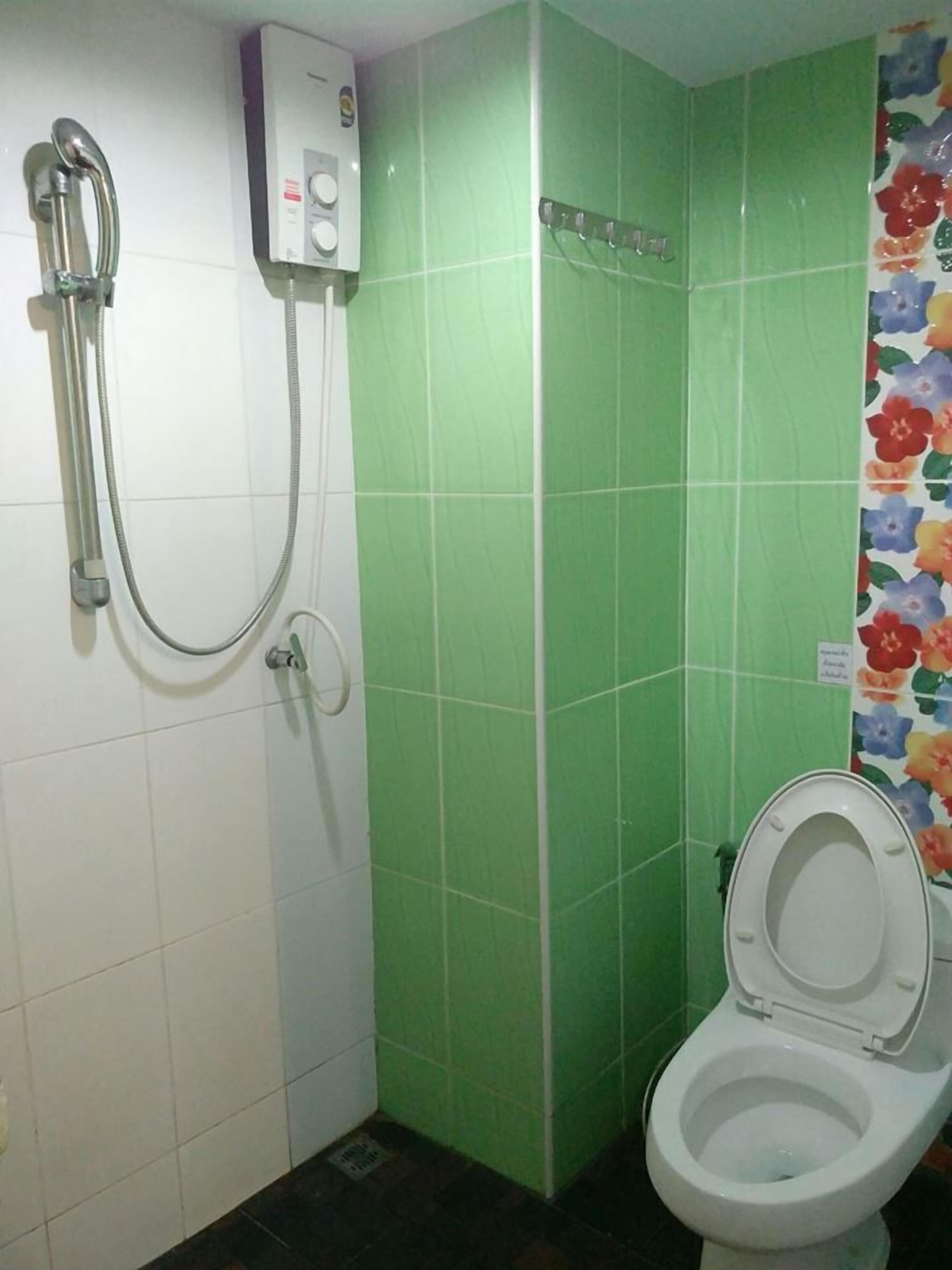 A bathroom with a toilet, a shower, and green tiled walls.
