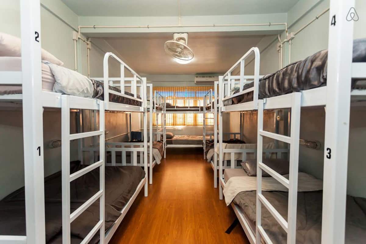 Une chambre de dortoir avec des lits superposés, un plancher en bois et un ventilateur de plafond.