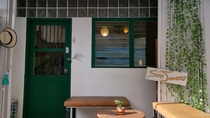 A wooden bench and table outside a building with a green door and window.