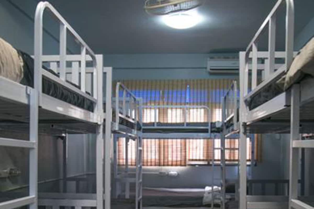 Une chambre avec trois lits superposés, un plancher en bois et une fenêtre avec des rideaux.