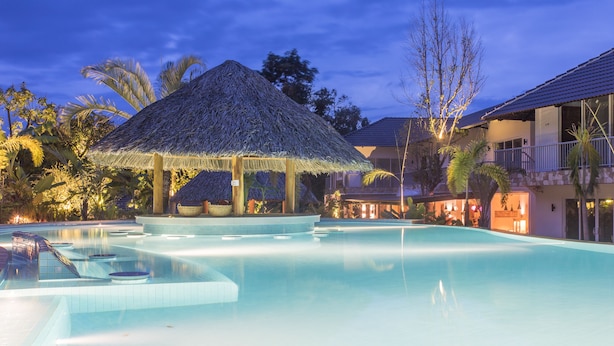 A swimming pool with a thatched gazebo, palm trees, and a building with a balcony. - Le Forest Resort (Phu Quoc)