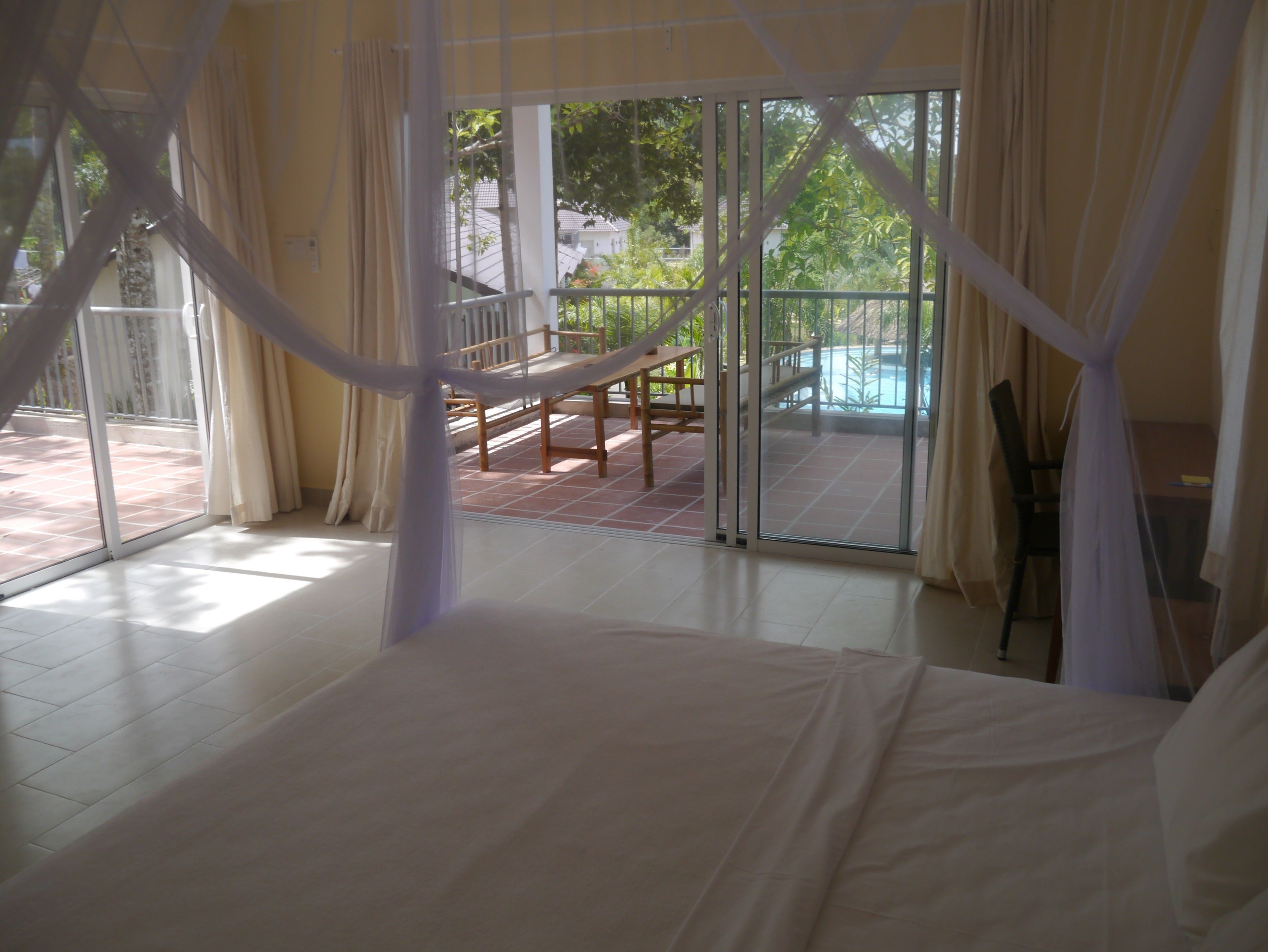 A bedroom with a large bed, a balcony with a hammock, and a view of a swimming pool.