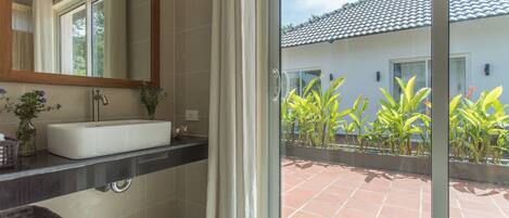 A bathroom with a large mirror, a white sink, and a window with curtains.