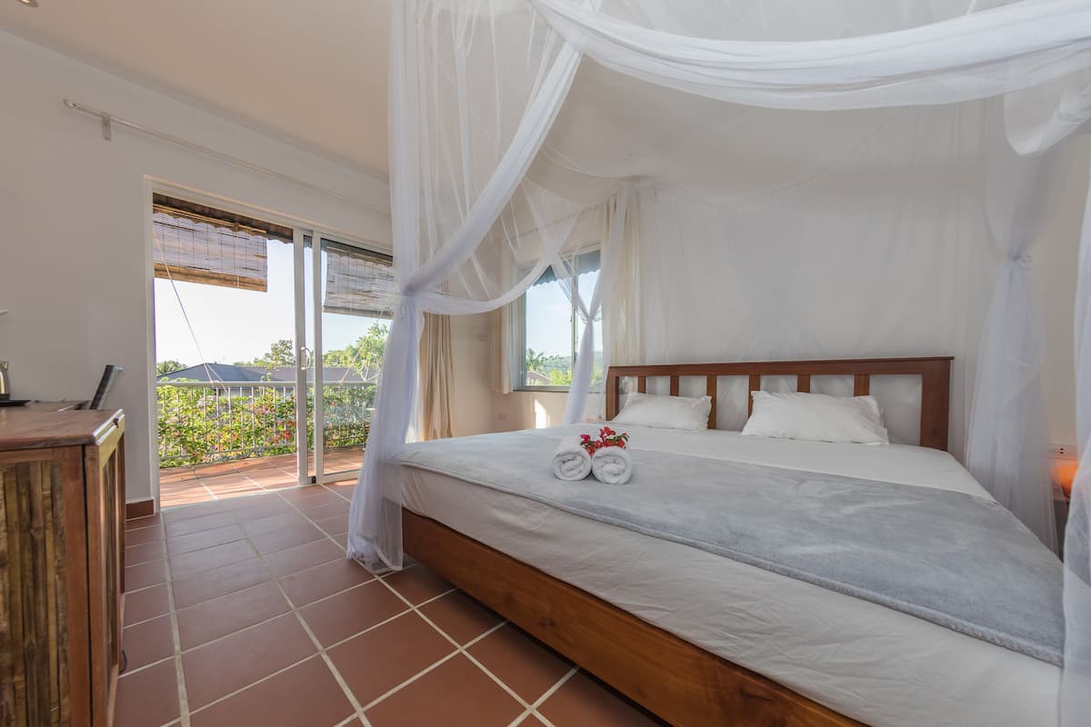 A bedroom with a large bed, a wooden headboard, and a balcony with a view.