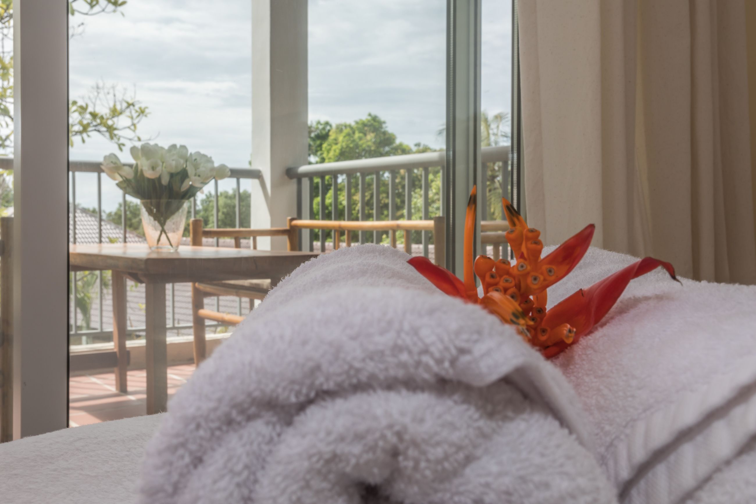 A hotel room with a balcony, a white towel, and a vase with flowers.