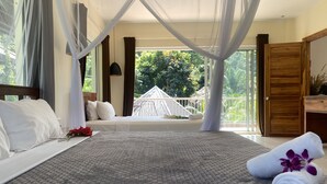 A bedroom with a large bed, a balcony with a view of greenery, and a wooden door. - Le Forest Resort (Phu Quoc)