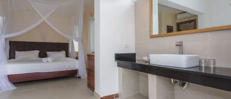A bedroom with a canopy bed, a bathroom with a black countertop and a mirror, and a tiled floor.