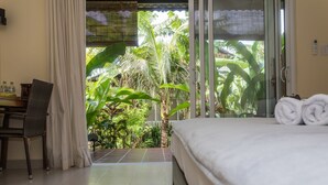 A hotel room with a bed, a desk with a chair, and a view of lush greenery through a glass door. - Le Forest Resort (Phu Quoc)