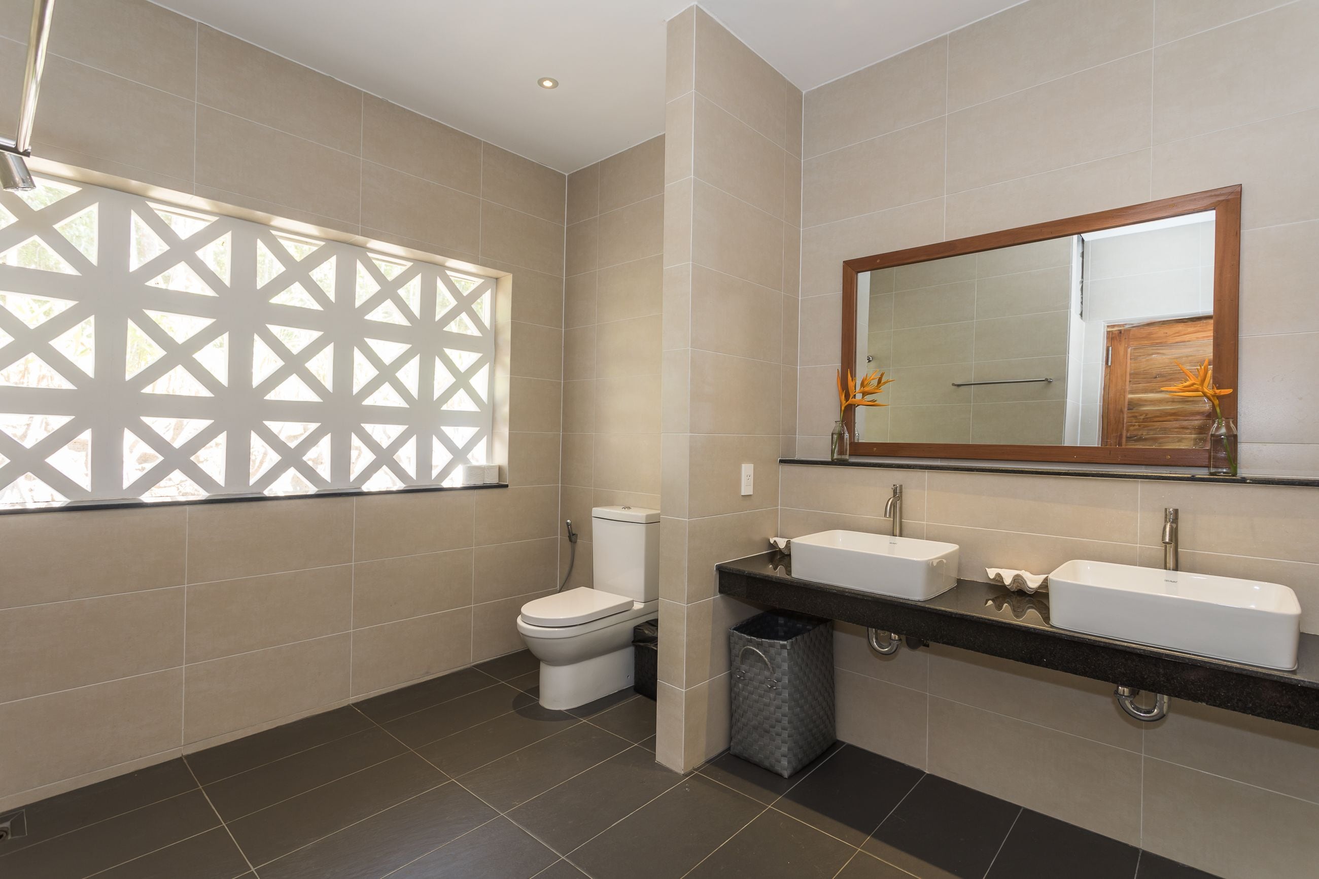 Et moderne badeværelse med toilet, to vaske, et spejl og et vindue med geometrisk mønster.