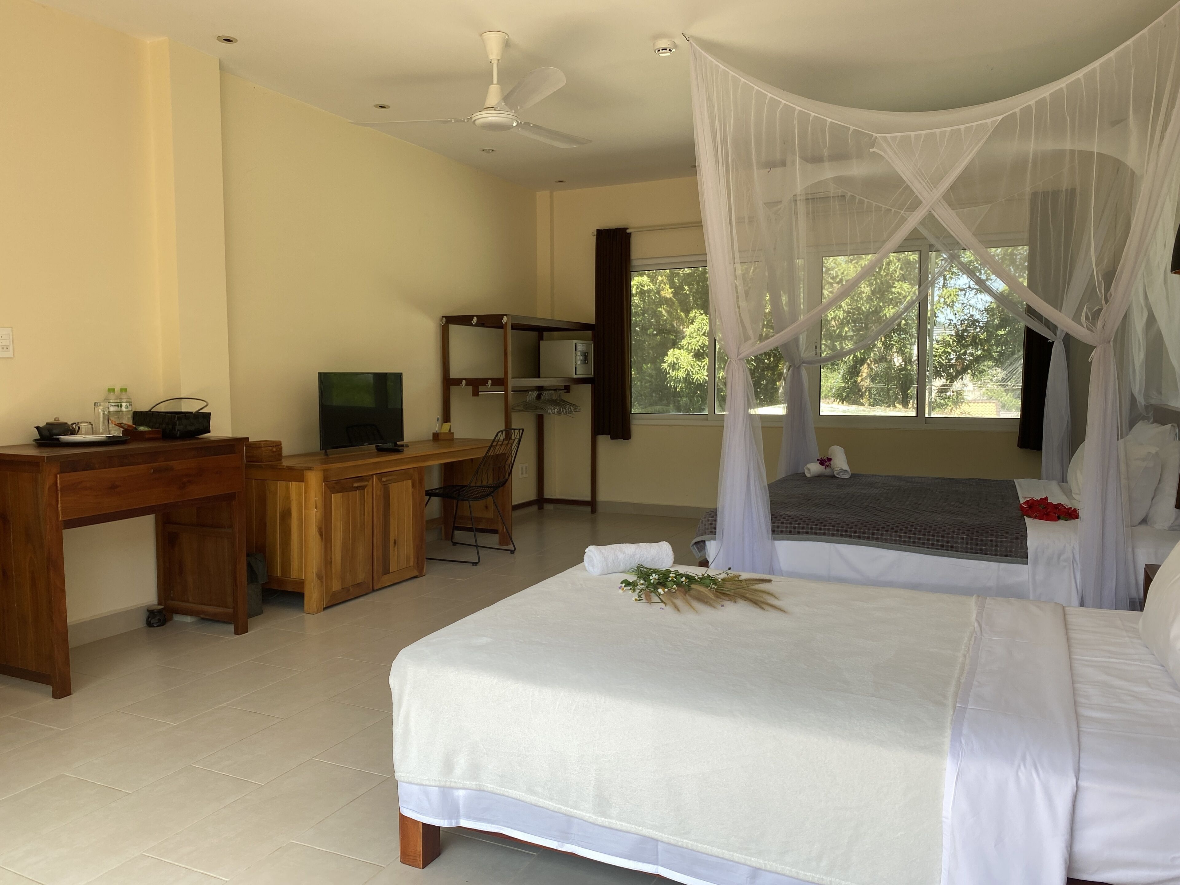 A bedroom with a bed, a desk, a chair, a television, and a window with a view of trees.