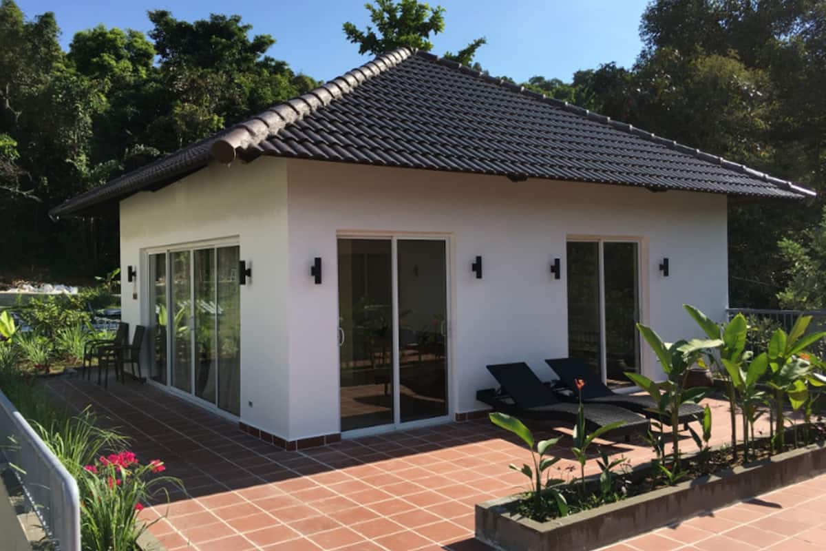A small, single-story building with a tiled roof, large sliding glass doors, and a patio area with outdoor seating.