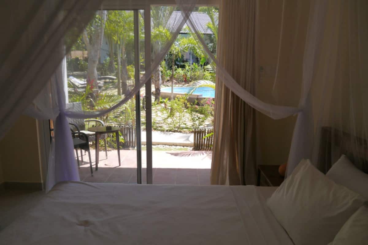 A bedroom with a bed, curtains, and a view of an outdoor area with a table and chairs.