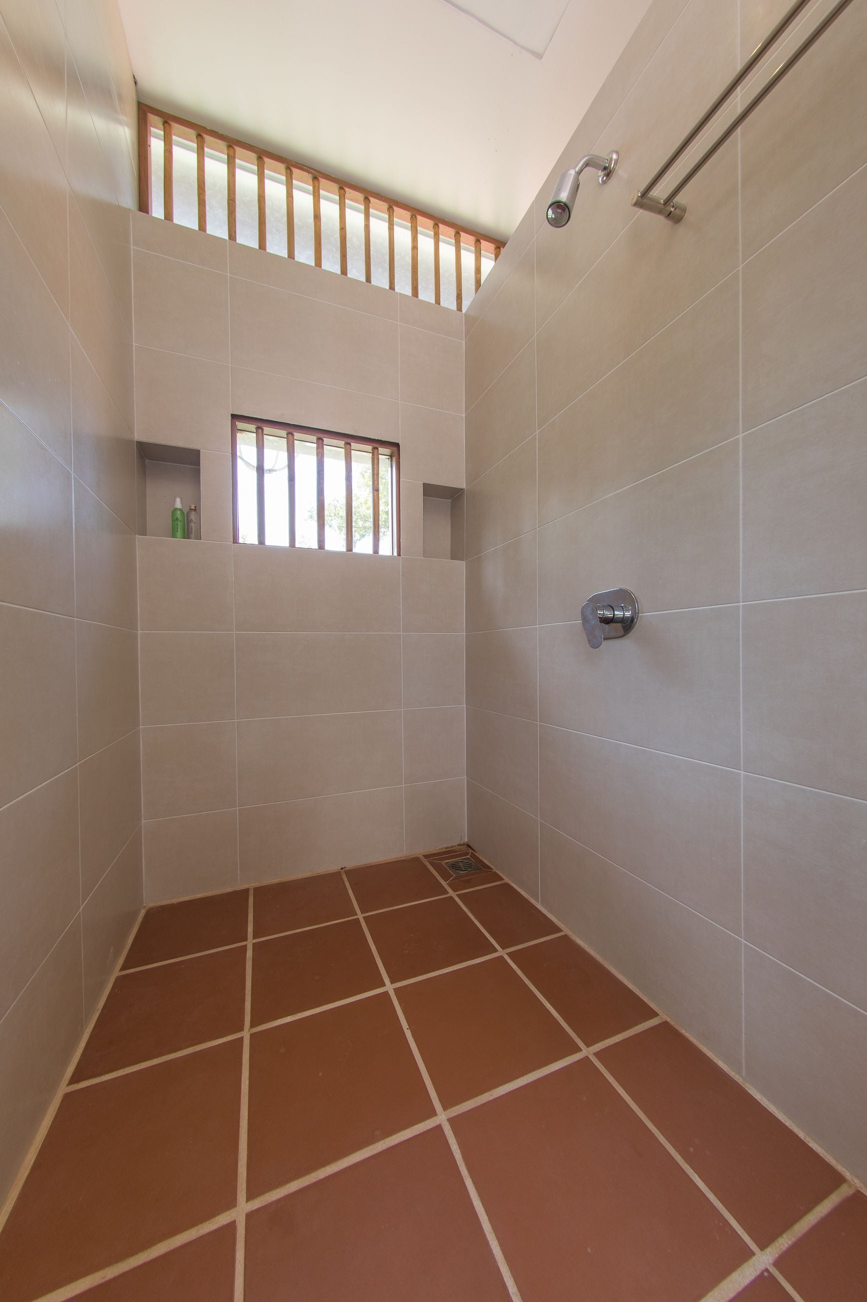 A bathroom with white tiles, a shower, and a window with bars.