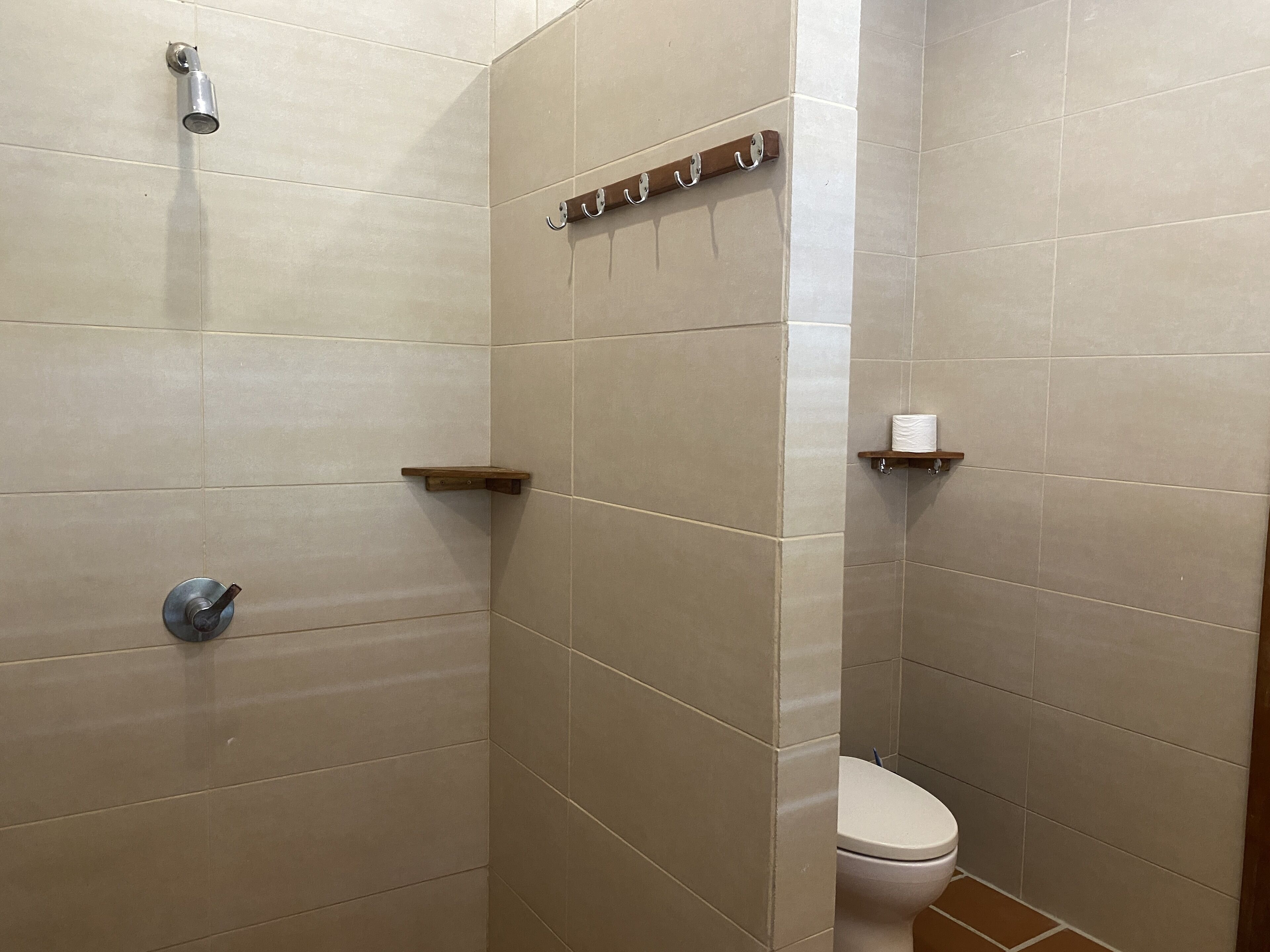 A bathroom with beige tiles, a shower, a toilet, and a towel rack.