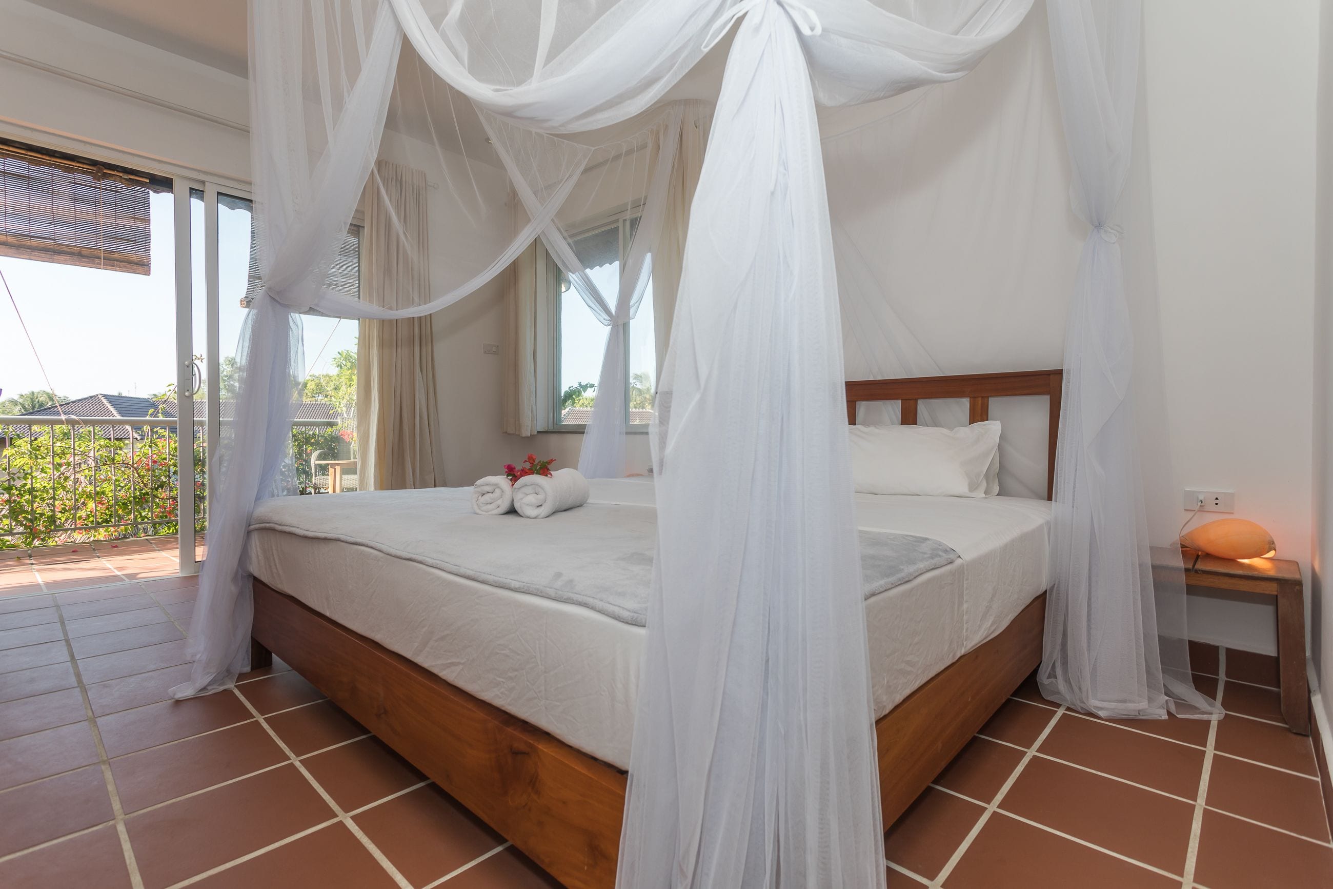 A bedroom with a bed, white curtains, and a view of the outside.
