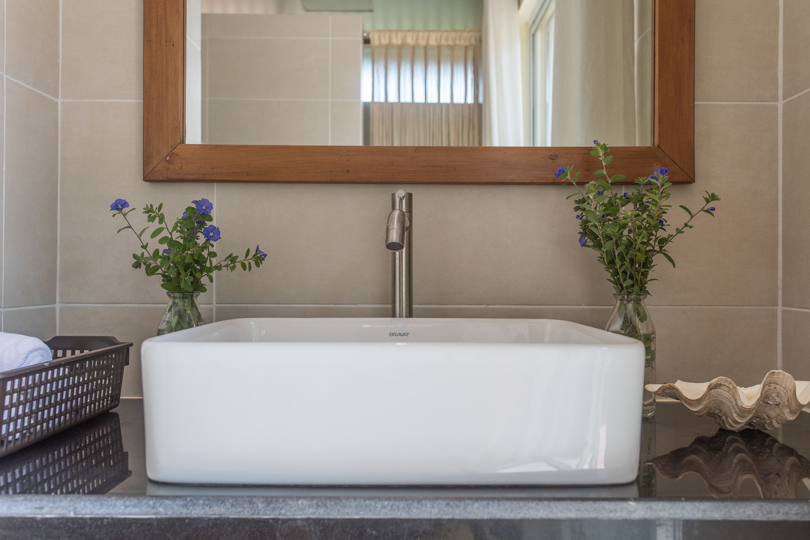 A bathroom with a rectangular white sink, a wooden-framed mirror, and two small vases with blue flowers.
