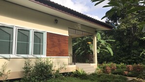 Une maison moderne avec un bardage en bois sur le côté, un balcon doté d’une rambarde en métal et une végétation luxuriante tout autour.