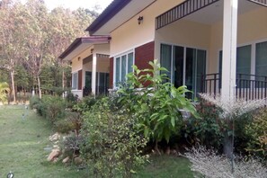 Una casa a due piani con un balcone, immersa in un giardino curato con diverse piante e un prato.