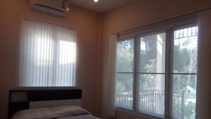 Une chambre à coucher comprenant un lit, un climatiseur, une fenêtre avec des stores et une vue sur l’extérieur.