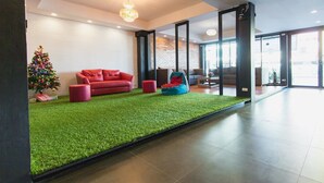 A modern living room with a red sofa, a green artificial grass area, and a Christmas tree. - Coconut Budget and Boutique Huahin (Hua Hin)