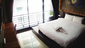 A hotel room with a large bed, a view through the window, and a painting on the wall. - Coconut Budget and Boutique Huahin (Hua Hin)